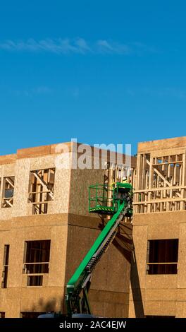 Construction worker elevated in hydraulic platform working on building with blue sky in background Stock Photo