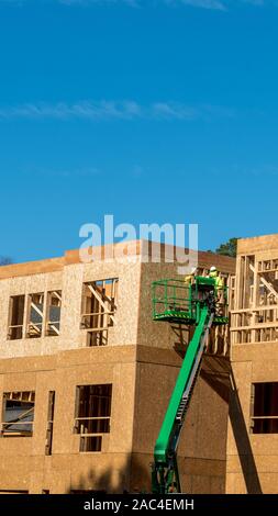 Construction worker elevated in hydraulic platform working on building with blue sky in background Stock Photo