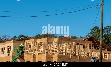 Construction worker elevated in hydraulic platform working on building with blue sky in background Stock Photo