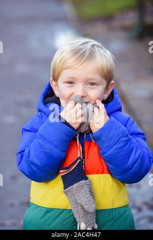 Hide and seek The boy is playing outside in outdoor clothing he is covering face and hiding while looking at the camera Stock Photo