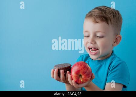 Portrait happy, smiling boy choosing junk food. Healthy versus unhealthy food. Healthy vs unhealthy eating, teenager choosing between cookie or an app Stock Photo