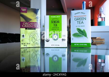 Boxes of Trader Joe's brand organic green tea, organic sencha tea, and decaffeinated green tea on a glass table. Stock Photo