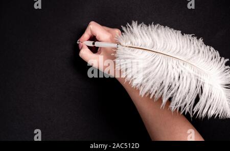 Female hand holding feather pen over black background Stock Photo
