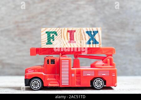 Red fire truck hold letter block in word fix on wood background Stock Photo