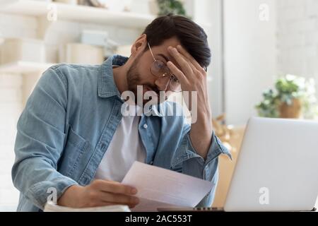 Upset frustrated young man holding reading postal mail letter Stock Photo