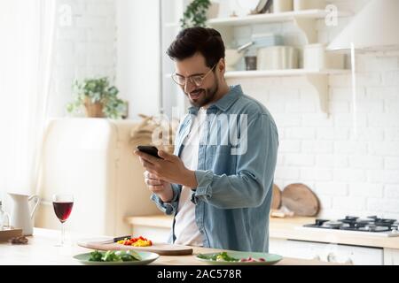 Happy young man preparing romantic dinner using smartphone app Stock Photo
