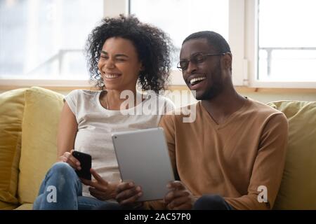 Overjoyed african American couple laugh watching funny video on tablet Stock Photo