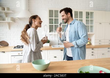 Funny couple singing in kitchenware microphones having fun in kitchen Stock Photo