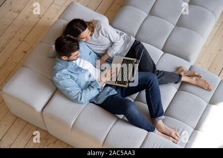 Happy young couple using laptop relaxing on sofa, top view Stock Photo