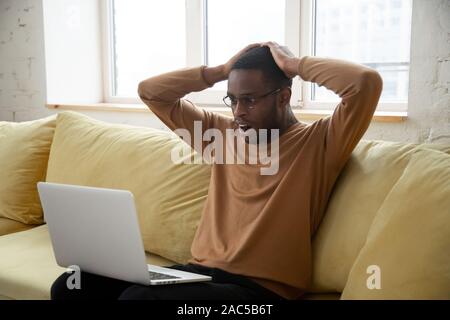 African American man shocked by online news on laptop Stock Photo