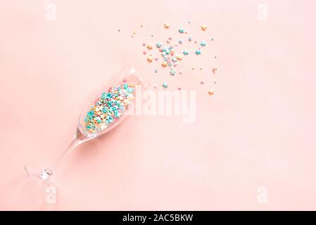 Champagne glass with colorful sugar sprinkles on pink background. Holiday, party and celebration concept. Creative flat lay with copy space. Stock Photo