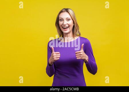 Good job! Portrait of extremely happy woman in tight purple dress showing thumbs up and smiling broadly at camera, overjoyed excited expression. indoo Stock Photo