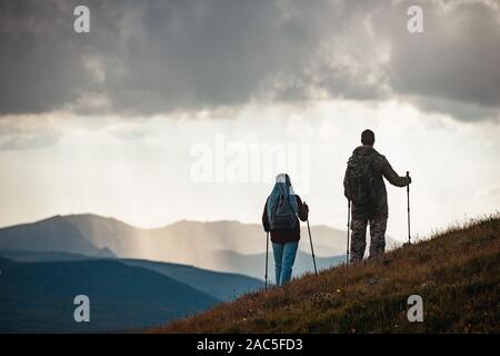 Couple of unrecognised hikers silhouettes stands with trekking poles in mountains