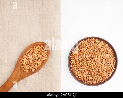 Buckwheat groats in clay plate and in wooden spoon on gray fabric and white background. Weight loss concept Stock Photo