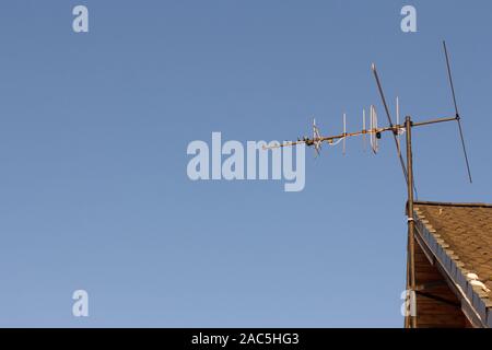 TV analog antenna on the roof of the house, against the blue sky Stock Photo