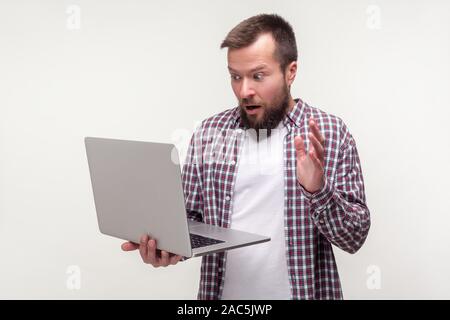 Portrait of frustrated bearded man in casual plaid shirt removes hand from laptop keyboard and looks scared about software failure, program bug. indoo Stock Photo