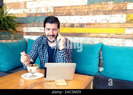 Remote working freelancer talking on phone in cafe while using digital tablet Stock Photo