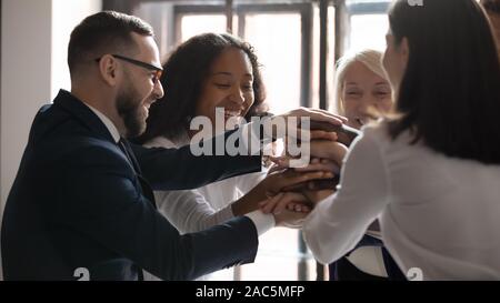 Happy mixed race mature and young coworkers stacking hands together. Stock Photo