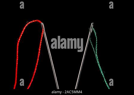a macro shot of the eye end of 2 steel sewing needles in a V, threaded with Red and Green thread on a black background with room for copy at center Stock Photo