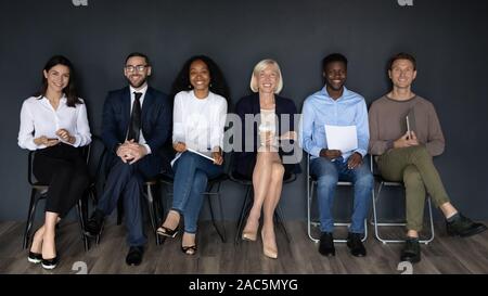 Full length diverse smiling business people sitting in line on chairs. Stock Photo