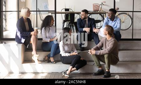 Joyful diverse older and young colleagues sitting on stairs. Stock Photo