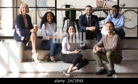 Portrait of happy mature and young coworkers sitting on stairs. Stock Photo