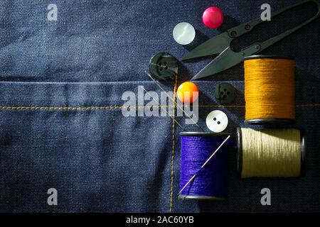 Needle and threads against plastic button and thread cutting scissors on jeans fabric. Top view and copy space for text. Concept of tailor or Designer Stock Photo