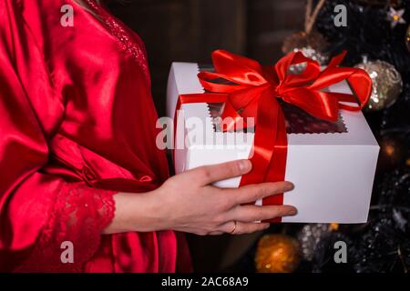 Christmas gifts, girl in red dress holds her hand on the carton, close-up Stock Photo