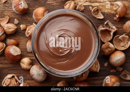 Chocolate spread or nougat cream with hazelnuts in glass jar on wooden background, copy space Stock Photo