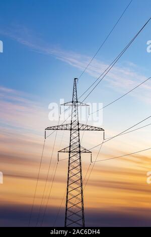 Silhouette of electricity pylon at sunset sky background. Stock Photo