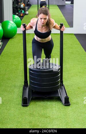 Young female fitness trainer performing sled push in local gym. Stock Photo