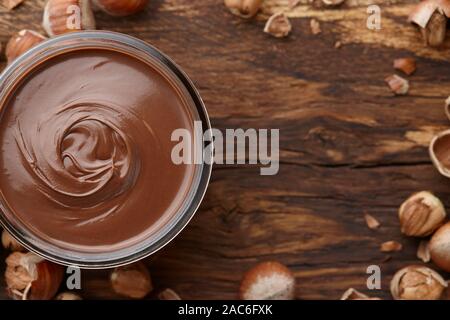 Chocolate spread or nougat cream with hazelnuts in glass jar on wooden background, copy space Stock Photo