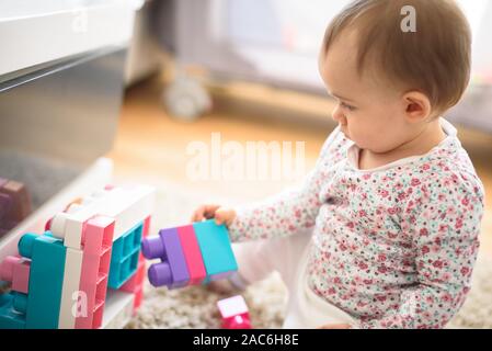 Beautiful baby building with plastic blocks in bright room. Education concept. 6 - 12 month old child. Stock Photo