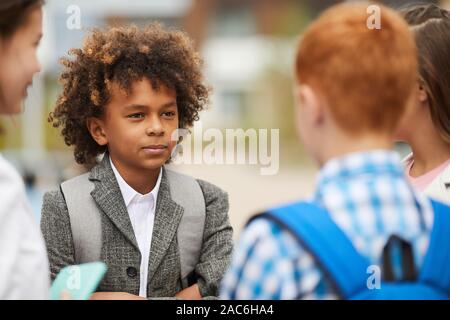 African schoolboy with curly hair standing and talking to his friends outdoors after school lessons Stock Photo