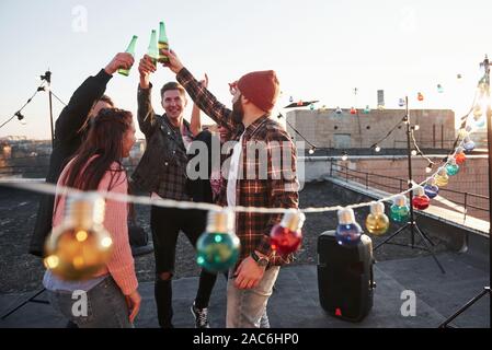 Unity of people. Holidays on the rooftop. Cheerful group of friends raised their hands up with alcohol Stock Photo