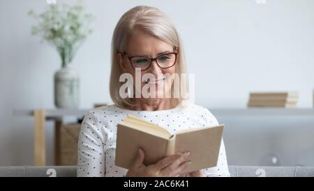 Elderly woman in glasses reading new book Stock Photo