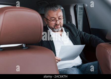 Paperwork on the back seat of the car. Senior businessman with documents Stock Photo