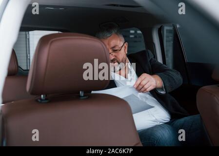 Reading contract. Paperwork on the back seat of the car. Senior businessman with documents Stock Photo