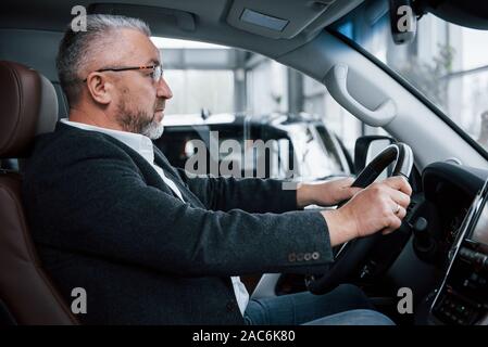 In black jacket. Senior businessman in official clothes trying new luxury car in auto saloon Stock Photo