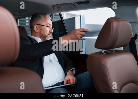 Receiving the contract. Paperwork on the back seat of the car. Senior businessman with documents Stock Photo