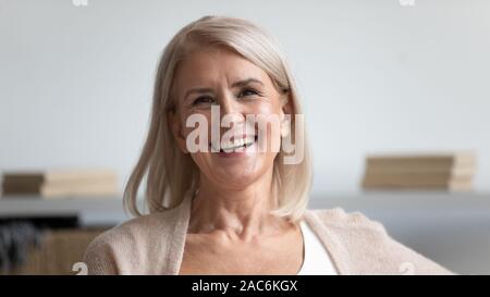 Attractive 60s female with wide charming candid smile posing indoors Stock Photo
