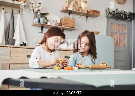Leisure time when parents is not at home. Two kids playing with yellow and orange toys in the white kitchen Stock Photo