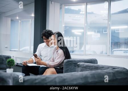 Coworkers in the office smiling and watching some funny stuff on the smartphone Stock Photo