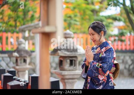 Geishas girl wearing Japanese kimono among red wooden Tori Gate at Fushimi Inari Shrine in Kyoto, Kimono is a Japanese traditional garment. The word ' Stock Photo