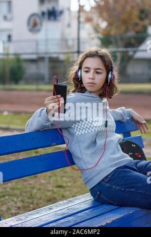Young beautiful fashionable teenager girl listens to music on headphones from smartphone Stock Photo