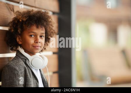 Portrait of African boy with curly hair and with headphones looking at camera while standing outdoors Stock Photo