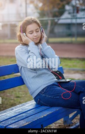 Young beautiful fashionable teenager girl listens to music on headphones from smartphone Stock Photo