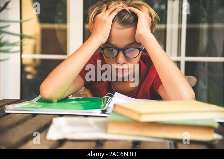 Tired student doing homework at home sitting outdoor with school books and newspaper. Boy weary due to heavy study. Kid asleep on the copybook Stock Photo