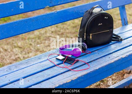 Headphones with smartphone and a black backpack on a blue park bench Stock Photo
