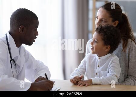 Young african american male pediatrician listening to little patient complaints. Stock Photo